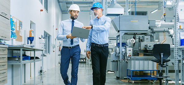 Two guys walking through factory looking at computer