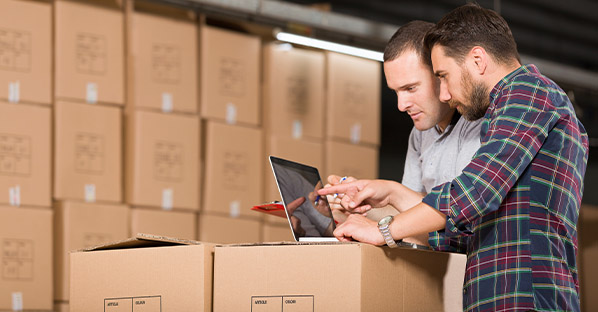 Two men in packaging warehouse looking at laptop